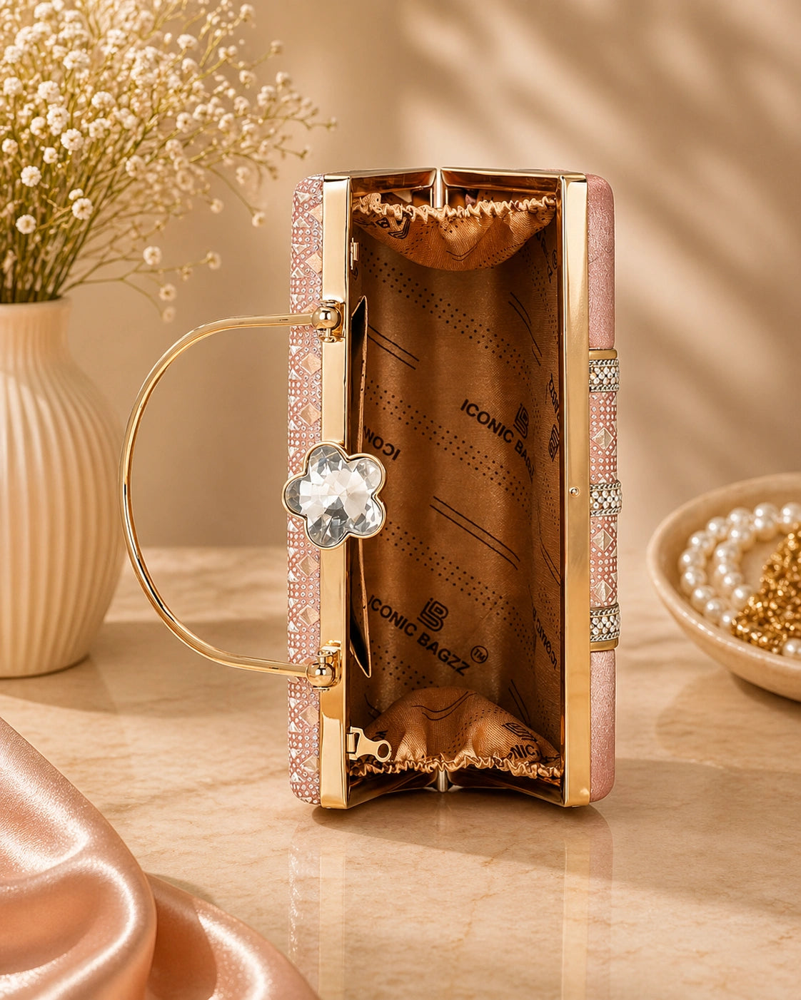 Rose gold handbag with decorative elements on a wooden surface with flowers and jewelry in the background
