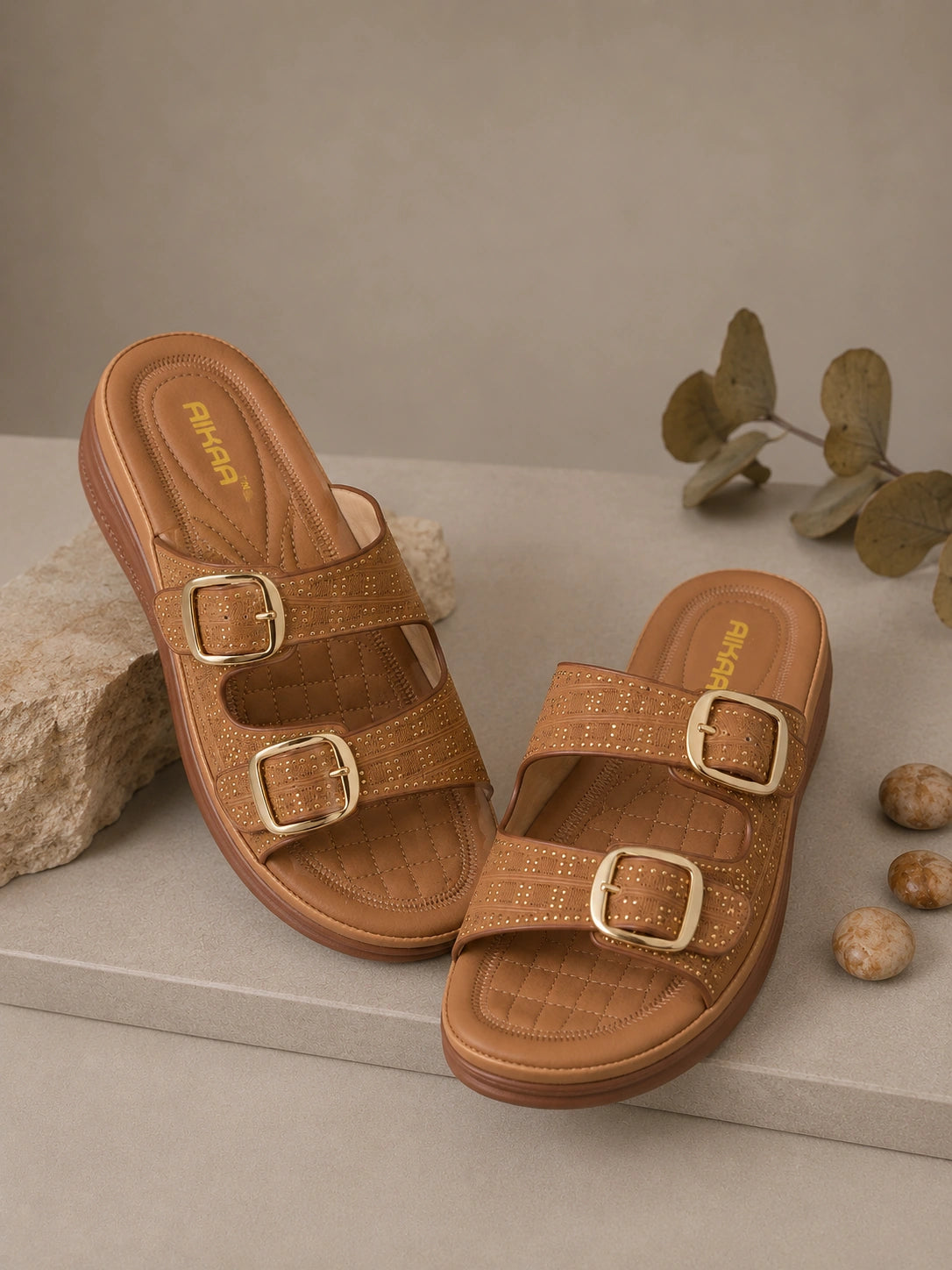 Pair of brown sandals with gold buckles on a neutral background
