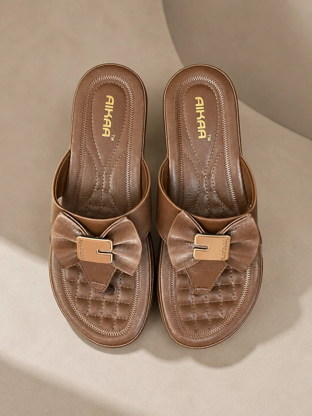 Pair of brown sandals with bow details on a beige background