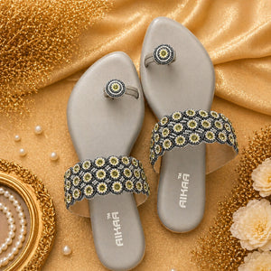 Silver sandals with floral embellishments on a gold fabric background