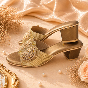 Gold high-heeled shoes with decorative elements on a beige fabric background