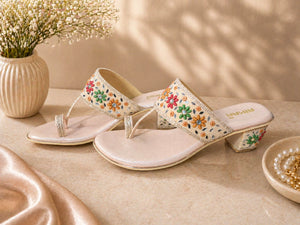Decorative sandals with floral patterns on a beige surface with a vase of flowers in the background.