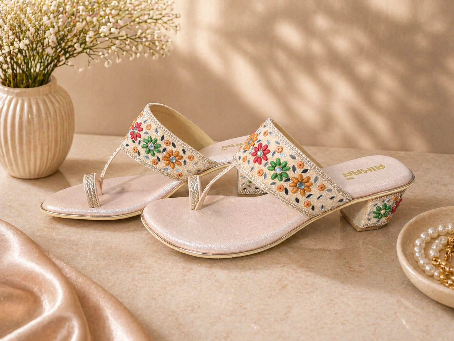 Decorative sandals with floral patterns on a beige surface with a vase of flowers in the background.